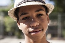 Портрет молодого хлопчика в солом'яному капелюсі, що стоїть на відкритому повітрі і дивиться на камеру — стокове фото