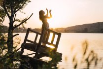 Женщина, стоящая на затонувшем пирсе у озера при солнечном свете — стоковое фото