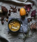Kürbiscremesuppe serviert in Schüssel mit Zutaten auf rustikalem Stoff mit Herbstblättern — Stockfoto