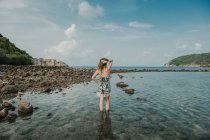 Frau im Sommerkleid steht am felsigen Ufer auf See in Thailand — Stockfoto