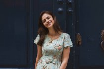Hübsche junge Frau im gemusterten Sommerkleid steht vor uralter Tür — Stockfoto