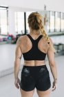 Vue arrière de l'athlète féminine avec les mains couvertes de craie debout dans la salle de gym pendant l'entraînement — Photo de stock