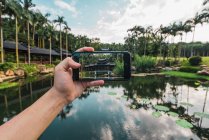 Human hand taking photo with smartphone of oriental building on tropical lake of Qingxiu Mountain, China — Stock Photo