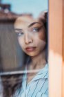 Junge ernsthafte brünette Frau schaut durch das Fenster — Stockfoto