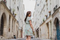 Vista trasera de mujer joven en lindo vestido de verano con estampado floral caminando por la calle y mirando por encima del hombro - foto de stock