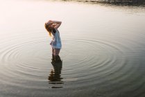 Woman standing in clear water of lake and touching hair — Stock Photo