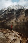 Vista lateral del turista adulto parado en el lago tranquilo en las montañas. - foto de stock