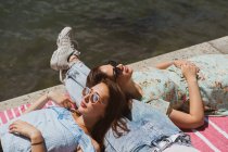 Sorridente amiche donne in occhiali da sole rilassante sul lungomare — Foto stock