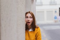 Здивована молода жінка спирається на стіну на вулиці — стокове фото