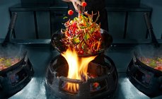 Ernte Hand Kochen Wok auf Pfanne über Feuer und Bewegung von Gemüse in der Luft — Stockfoto