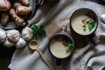 Ciotole di gustosa zuppa di topinambur con ingredienti su tavola rustica di legno — Foto stock