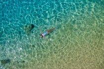 Повітряний вигляд жінки в яскравому купальнику, що лежить на поверхні бірюзової води — стокове фото