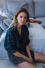 Молодая женщина в клетчатой огромной рубашке сидит на полу рядом с диваном и смотрит в камеру — стоковое фото