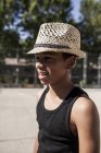 Усміхнений молодий хлопчик в солом'яному капелюсі стоїть на відкритому повітрі і дивиться в сторону — стокове фото