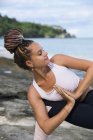 Jeune femme en forme étirant au bord de la mer pendant le yoga — Photo de stock