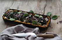 Tarte au four avec polenta et épinards garnie de morceaux de fromage crottin dans un plat de cuisson sur une table en bois — Photo de stock