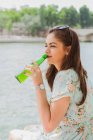 Young woman in summer dress drinking water at waterfront — Stock Photo