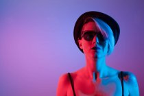 Atractiva mujer con sombrero de disparar en el estudio con luces azules y rojas - foto de stock