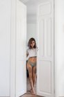 Tattooed woman in panties and T-shirt standing in doorway and closing doors in stylish apartment — Stock Photo