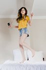 Девушка танцует в постели со смартфоном и наушниками — стоковое фото
