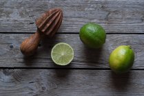 Limes fraîches entières et coupées en deux avec pressoir en bois sur bois gris — Photo de stock