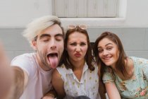 Smiling young women and man in casual clothes taking selfie outdoors — Stock Photo