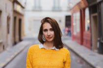 Pretty woman in yellow cardigan standing on street and looking at camera — Stock Photo