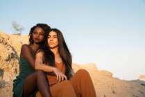 Dreamy elegant diverse girlfriends sitting on beach — Stock Photo