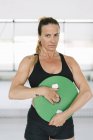 Спортсменка в черной спортивной одежде держит тяжелый диск и делает упражнения во время тренировки в тренажерном зале — стоковое фото