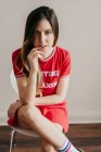 Hübsche Frau im roten Outfit sitzt auf Stuhl und starrt in die Kamera — Stockfoto