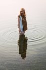 Woman standing in clear water of lake and looking down — Stock Photo