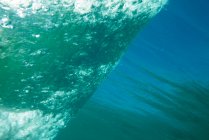 Подводный фон яркой бирюзовой волны с белыми пузырьками воздуха, катящимися по спокойной поверхности воды в океане — стоковое фото