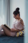 Зосереджена брюнетка жінка читає книгу на ліжку — стокове фото
