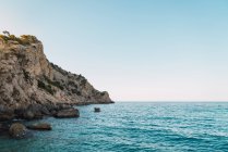 Panorama of clear blue sea water against rocky cliffs of shoreline and blue sky — Stock Photo