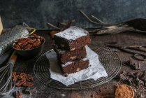 Morceaux de délicieux brownie au chocolat o n porte-fil avec des ingrédients sur la surface en bois sombre — Photo de stock
