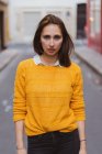 Красивая женщина в жёлтом кардигане стоит на улице и смотрит в камеру. — стоковое фото