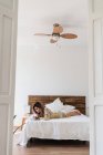 Молодая женщина в шелковом халате лежит на кровати и делает наброски в блокноте в стильной спальне — стоковое фото