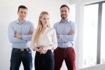 Gruppo di colleghi d'ufficio in piedi insieme rilassato con le braccia incrociate e guardando la fotocamera sorridente in camera spaziosa a parete di vetro e porta — Foto stock