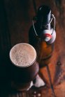 Толстое пиво в стекле и бутылка на темном деревянном столе — стоковое фото