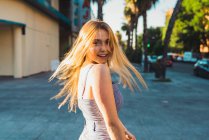 Young woman in stylish outfit looking at camera while standing on blurred background of street — Stock Photo