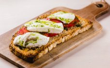Close-up of golden bread toast with tomatoes and white cheese topped with green sauce on wooden board — Stock Photo
