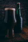 Cerveza en vidrio y botella en mesa de madera oscura - foto de stock