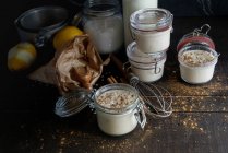 Стеклянные банки со сладким десертом риса с молоком и корицей на деревянном столе с ингредиентами — стоковое фото