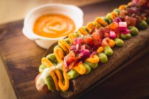 Primer plano de delicioso hot dog adornado con verduras y salsa sobre tabla de madera - foto de stock