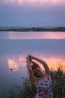 Чуттєва жінка в літній сукні, стоячи на березі озера на заході сонця — стокове фото