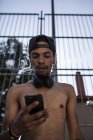 Menino afro ouvindo música com fones de ouvido e smartphone enquanto fuma na frente da grade — Fotografia de Stock