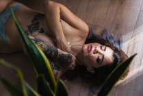 Mujer tatuada en topless cubriendo el pecho y acostada con los ojos cerrados en el suelo - foto de stock