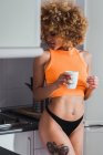 Sensuale donna in lingerie in possesso di tazza in cucina — Foto stock