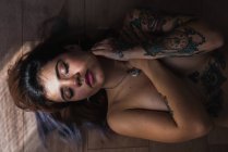 Topless mulher tatuada cobrindo o peito e deitado com os olhos fechados no chão — Fotografia de Stock