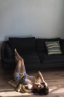 Barfüßige Frau im Seidenmantel, die Beine auf der Couch hält und auf dem Boden liegend in die Kamera schaut — Stockfoto